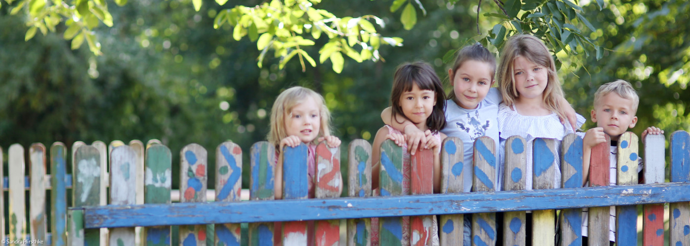 Einige Kinder stehen an einem bunt bemalten Zaun