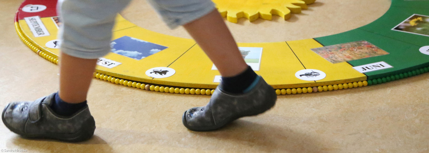 Ein kleines Kind aus einer Kita geht um eine Jahreszeitenuhr herum.