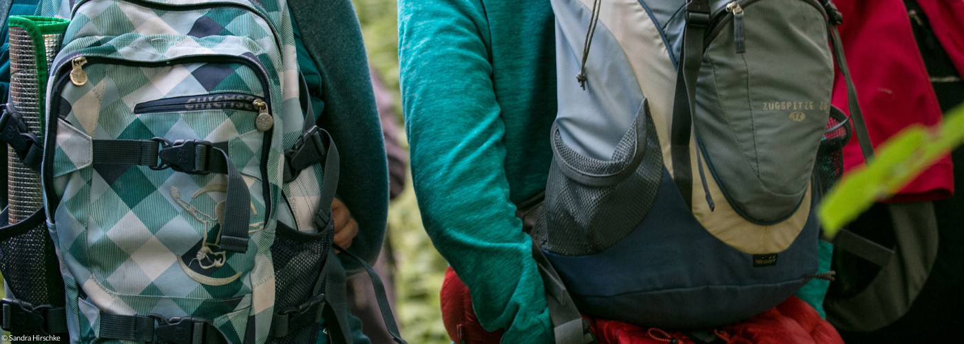 Drei Personen mit Wanderrucksäcken auf dem Rücken