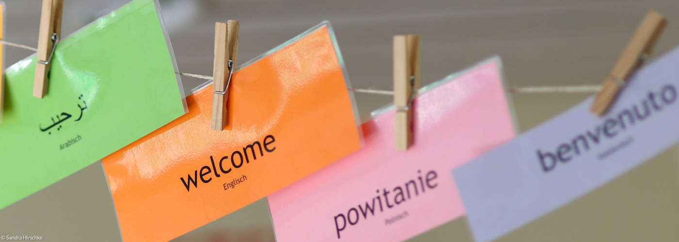 Willkommensschilder in verschiedenen Sprachen hängen an einer Leine