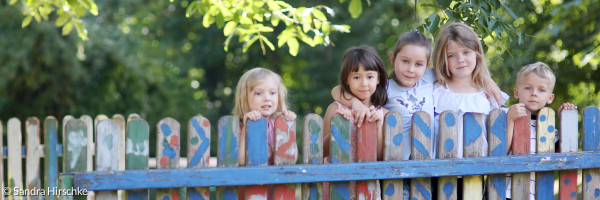 Einige Kinder stehen an einem bunt bemalten Zaun